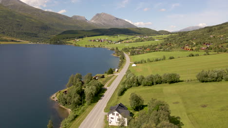 automóviles circulando por la carretera junto a la orilla del lago de eidsvatnet en eidsdal, noruega, con el pueblo de montaña de aarset al fondo