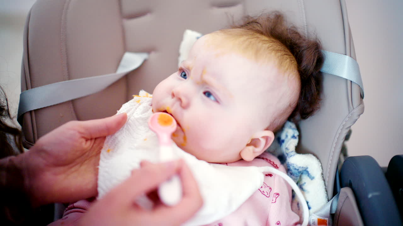 Close-up de um bebê sendo gentilmente alimentado com uma colher por um adulto.
