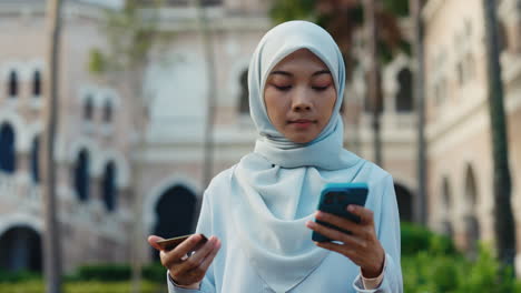 young muslim woman using smartphone and credit card outdoors