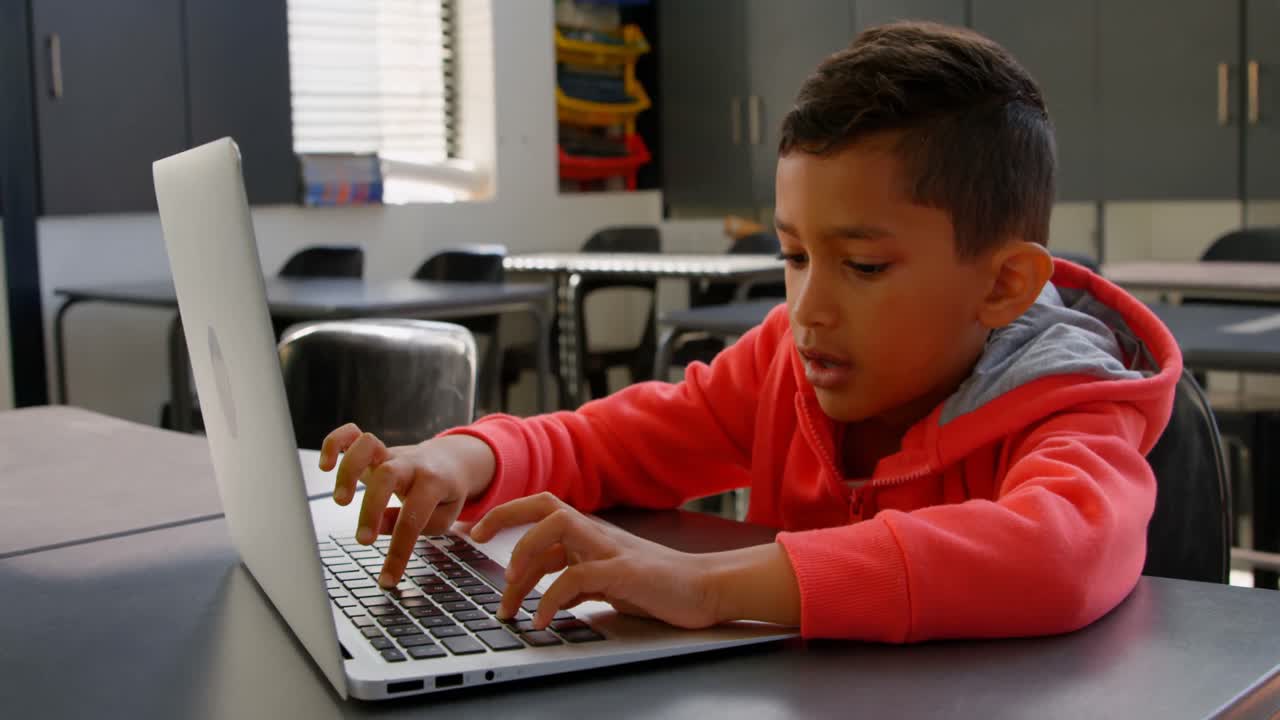 vista frontal de un escolar asiático atento estudiando con una computadora portátil en el aula de la escuela 4k