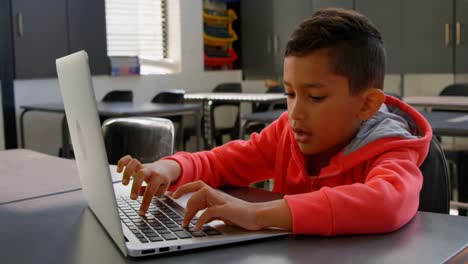 Front view of attentive Asian schoolboy studying with laptop in classroom at school 4k