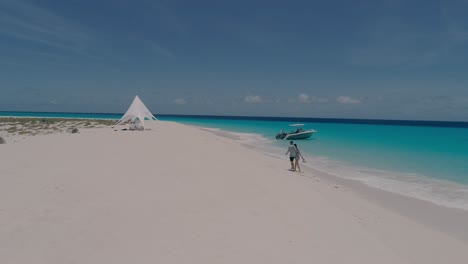 Pareja-Caminando-Descalza-En-La-Playa-Tropical-De-Arena-Blanca-Hacia-La-Tienda-De-Campaña,-Disparo-De-Drones