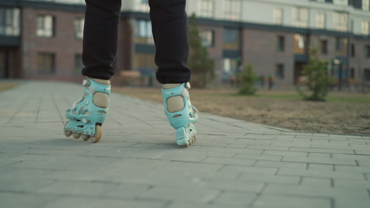 A close-up back shot of rollerblades gliding smoothly through a paved park path, with residential buildings visible in the background. focusing on the motion and the urban environment