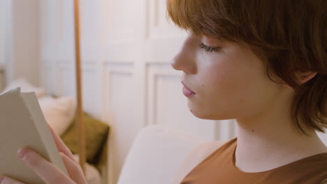 Close-Up-View-Of-Girl-Sitting-On-A-Chair-Reading-A-Book-In-The-Bedroom-1