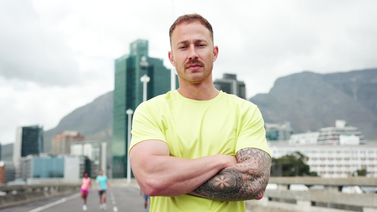 Zelfverzekerde mannelijke atleet staat met gekruiste armen in stedelijke omgeving.