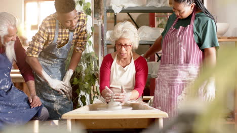 Happy-biracial-female-potter-with-others,-using-potter's-wheel-in-pottery-studio,-slow-motion