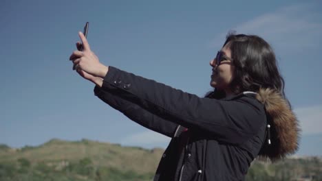 narrow shot of a girl taking selfie and pictures with blue sky and landscape in slow motion