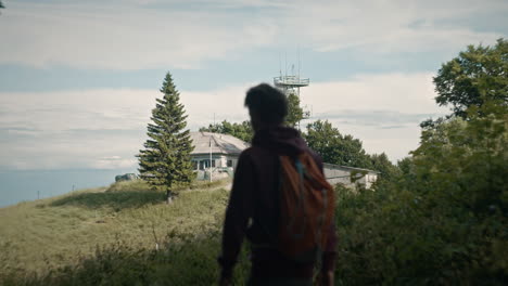 Joven-Excursionista-Despertando-Hacia-La-Cabaña-De-Montaña-Y-Una-Torre-De-Radio