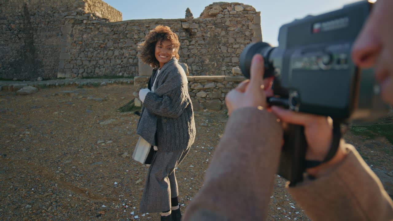 Photographer filming woman sunset shore closeup. Cheerful girl laughing at coast