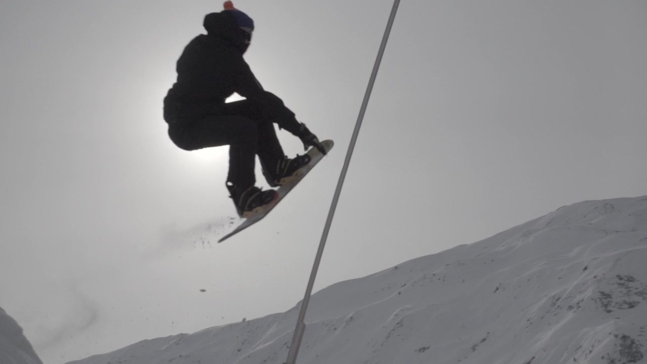 Slowmotion shot of a snowboarder jumping high in front of the sun and landing on an orange air cushion LOG