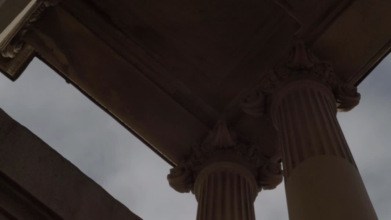 Looking up at ornate stone pillars and roof against blue skies panning
