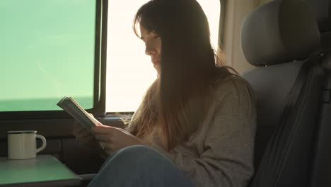 traveling woman reading book in van at sunset