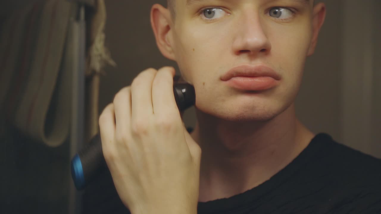 Mirror Reflection Of A Caucasian Guy Shaving With A Rechargeable Shaver - close up