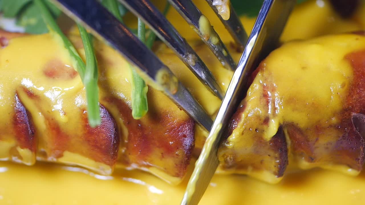 노란색 소스와 함께 소시지를 잘라내는 포크와 칼