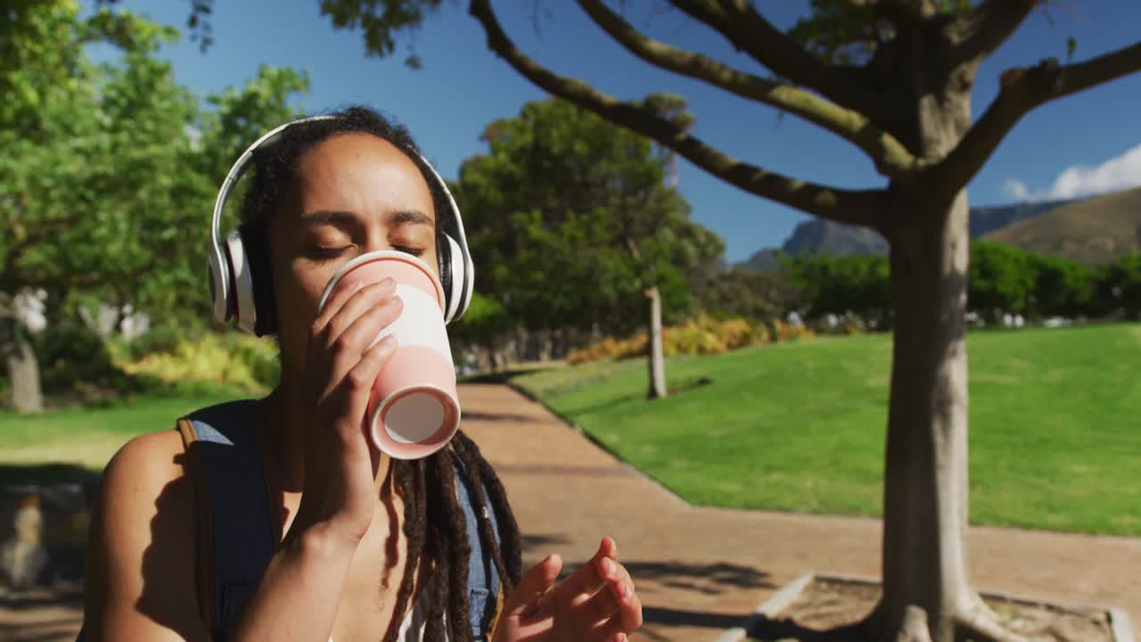 mujer afroamericana con auriculares sentada bebiendo café en el parque