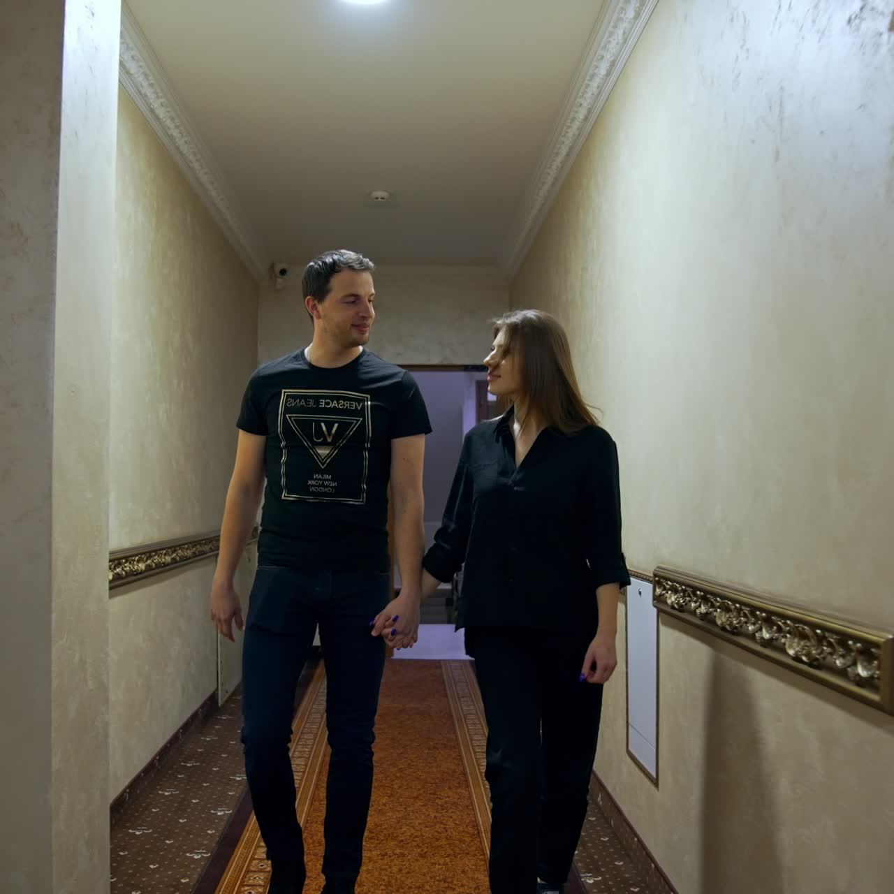 Couple walking by the corridor holding by the hands and talking. Man and woman go indoors by the long hall