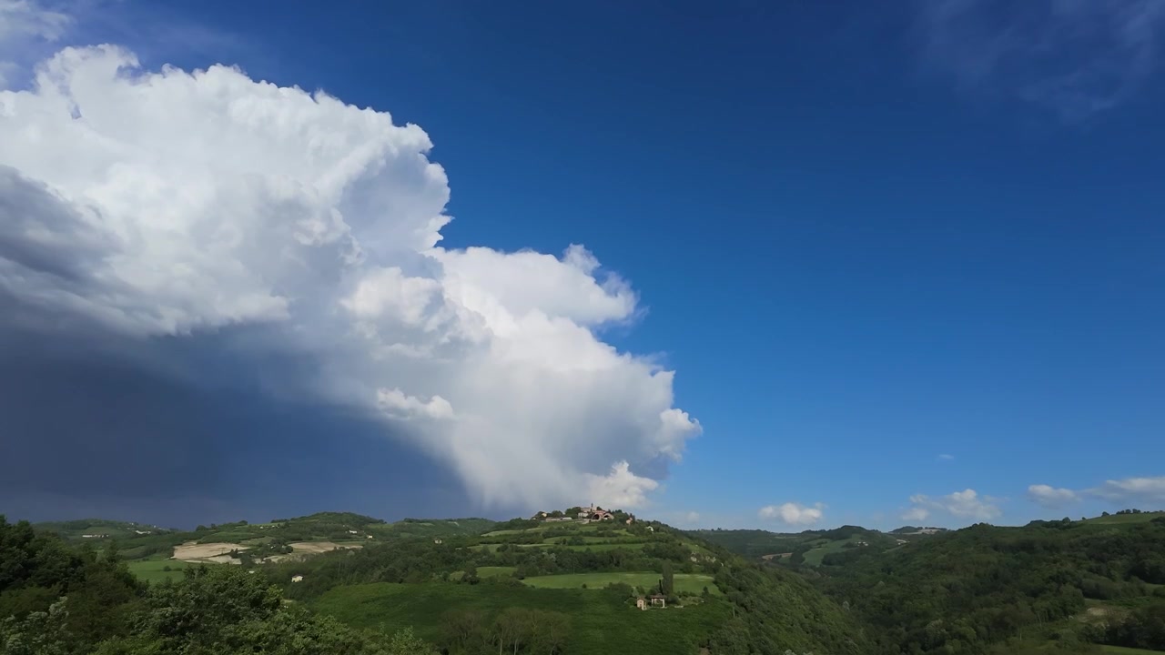 Wide angle timelapse captures dramatic storm clouds moving across rolling green hills and Italian vineyards
