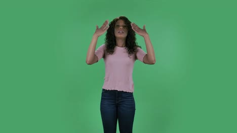 retrato de una hermosa mujer joven afroamericana está mirando derecho. ella tiene temperatura es tos y se cubre con un codo. morena ardiente con cabello ondulado en vaqueros y una blusa beige en una pantalla verde en el estudio. protección de la salud corona