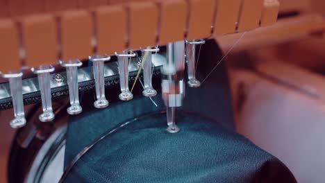 close up of embroidery machine needle stitching red thread into blue denim fabric in motion
