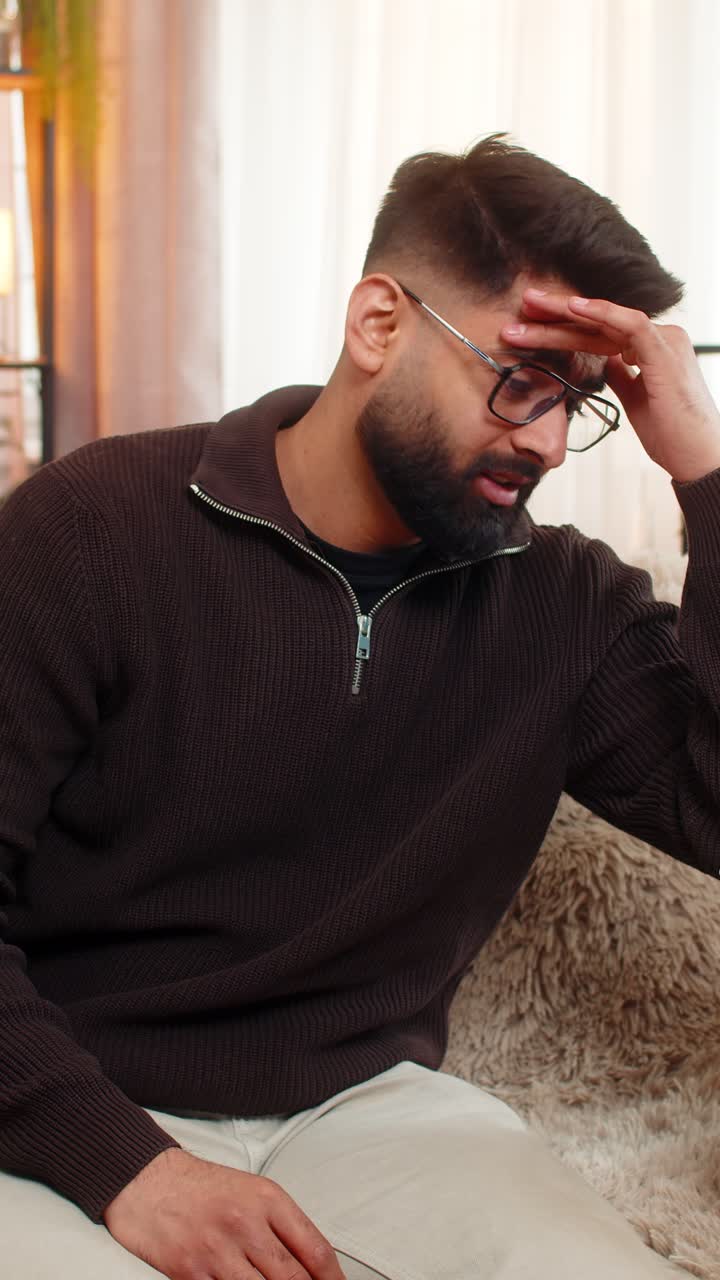 Indian man on sofa opens box and shakes head after discovering wrong item in online delivery order