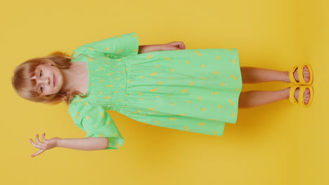 a young girl in a green dress is standing on a yellow background and smiling.