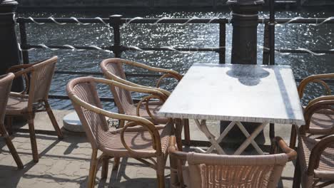 a panning shot of the empty chairs and tables at a street cafe on the riverside.