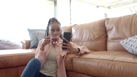 african american young woman holding tea, looking at phone