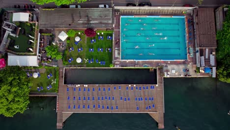 Top-down-people-swimming-in-pool-with-a-restaurant-and-dock,-Lake-Como