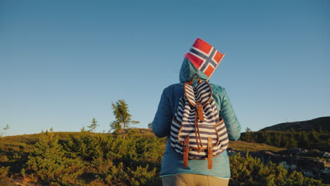 a tourist with a norwegian flag in a backpack walks through the picturesque highlands at dawn active