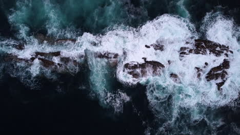 ocean waves breaking of partially submerged rock formation, aerial top down dolly in