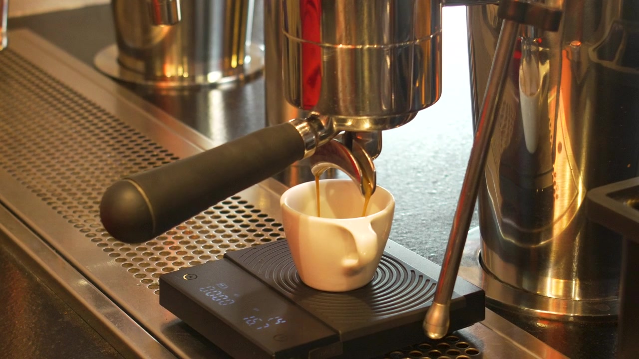 Preparazione artigianale di espresso con bilancia digitale e tazza bianca presso una postazione da barista professionale.