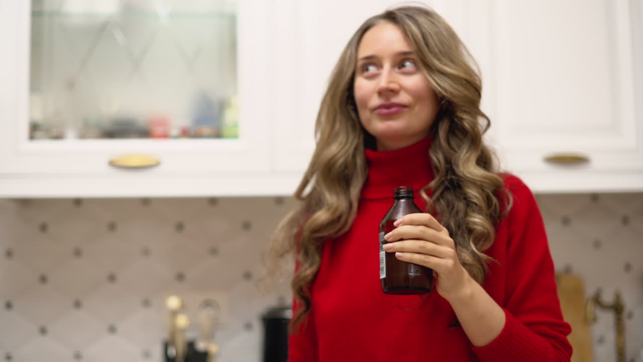 Woman drinking kombucha from a brown glass bottle in the kitchen