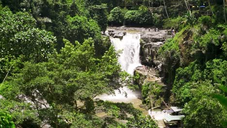 Wide-shot-of-distant-Tegenungen-Waterfall-partially-obscured-by-lush-greenery