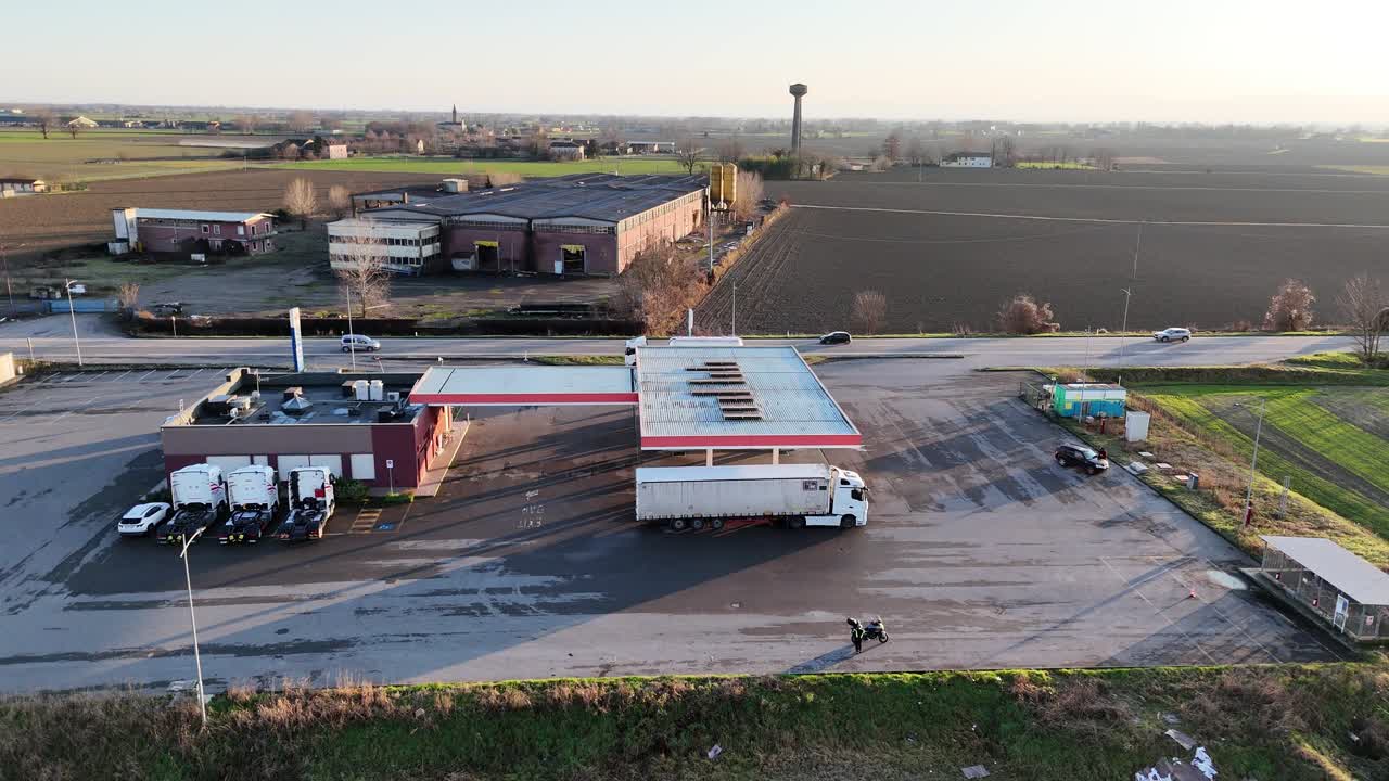 roadside gas station located along SS10 Strada Padana Inferiore, showing fuel canopy, service building, parking area, access road, and surrounding agricultural fields, aerial