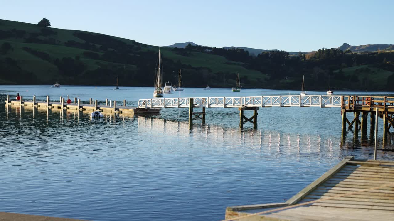 A serene view of a pier and calm waters in Akaroa, captured under clear skies with gentle lighting