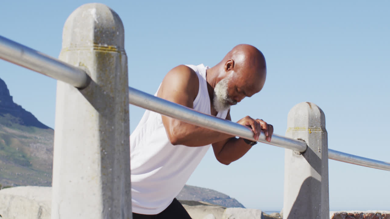 Senior african american man exercising stretching on rocks by the sea