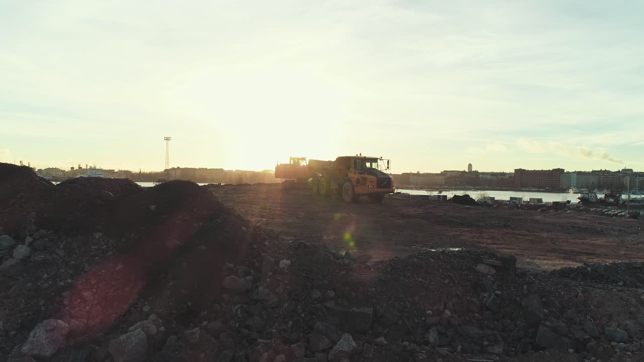 Statisk luftfoto af en gravemaskine, der graver og læsser jord i en lastbil med solnedgang i baggrunden
