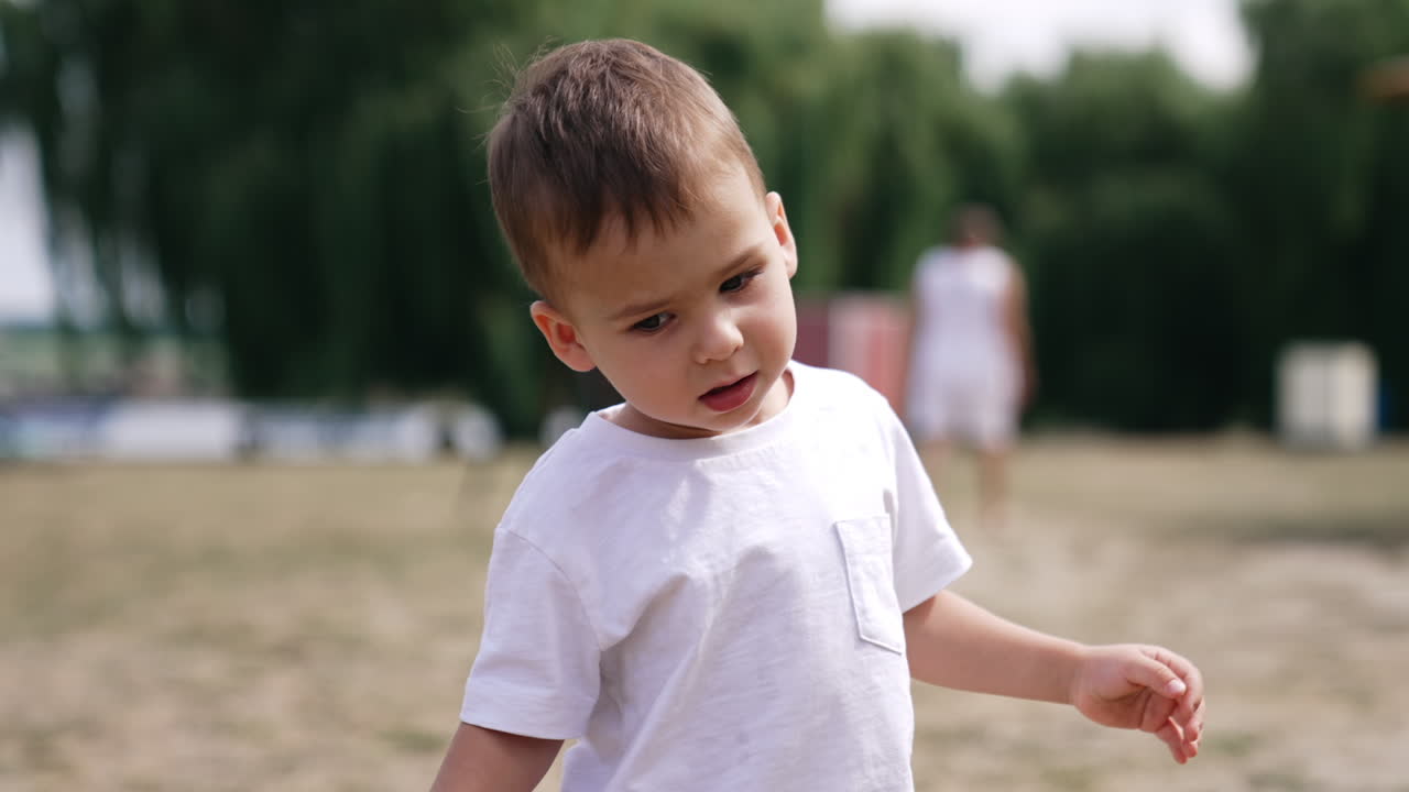 Adorable Caucasian kid bending head left and right. Portrait of a toddler outside in summer. Blurred backdrop.