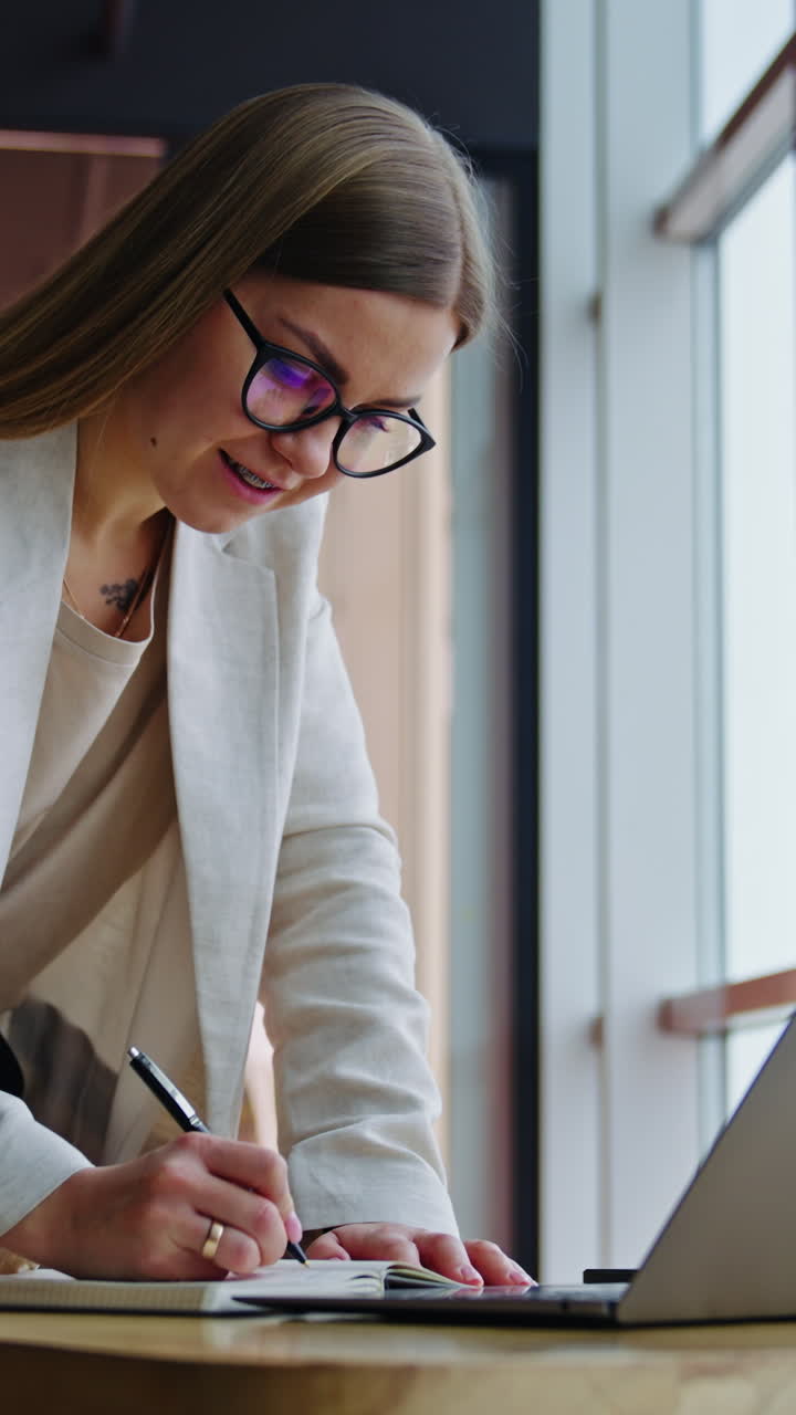 Office lady surfing the net and taking notes. Female employee standing leaned on the table in a spacious office. Vertical video