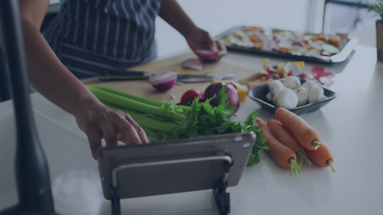 Home cook chopping onion for dinner at kitchen counter, causing hearts multiplying near tablet
