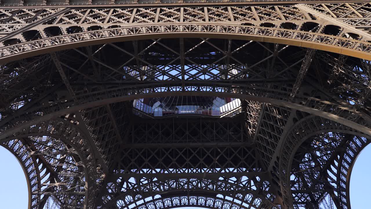 A slow panning view reveals the Eiffel Tower’s majestic structure from underneath on a sunny Parisian day, iconic architecture