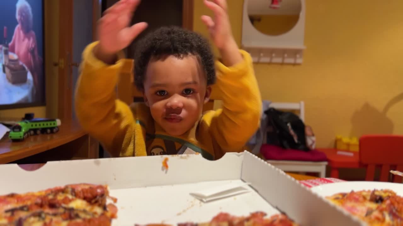 Expressive, sweet and funny two-year-old black baby fed by hir mother with pizza and home