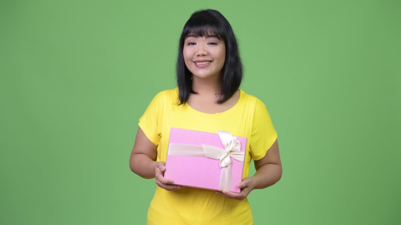 Beautiful happy Asian woman thinking while holding gift box
