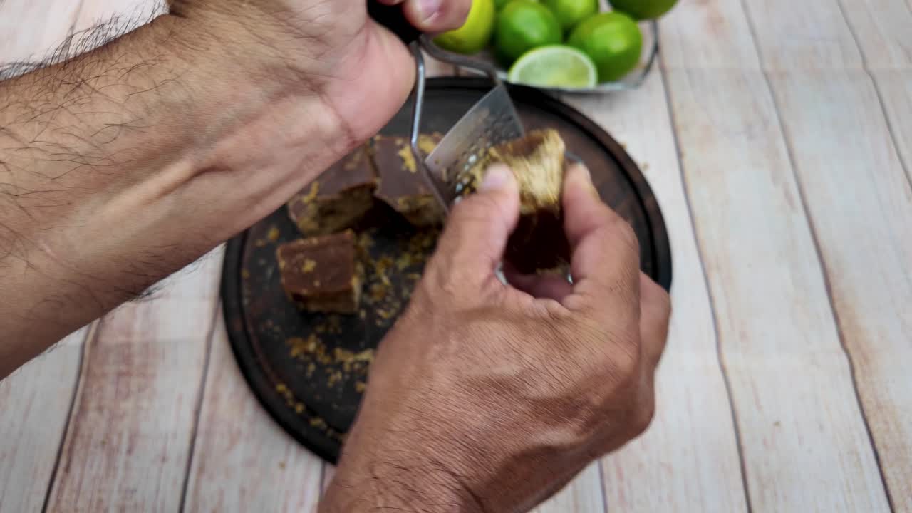 Primer plano de un proceso práctico y auténtico en el que se ralla un pequeño bloque de panela (caña de azúcar sin refinar) con un rallador metálico de mano, mostrando la textura del ingrediente y el trabajo manual.