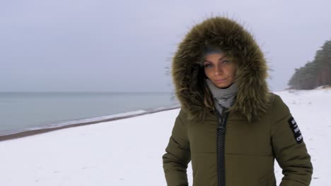 una joven vestida de verde con ropa de invierno camina por la orilla arenosa de la playa del mar báltico, un día nublado de invierno, un tiro de seguimiento medio manual a la derecha