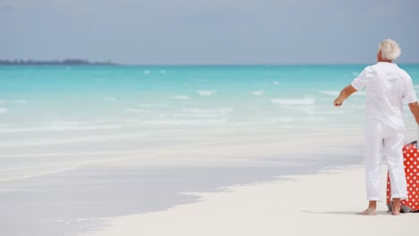 barefoot mature caucasian couple on beach with suitcase