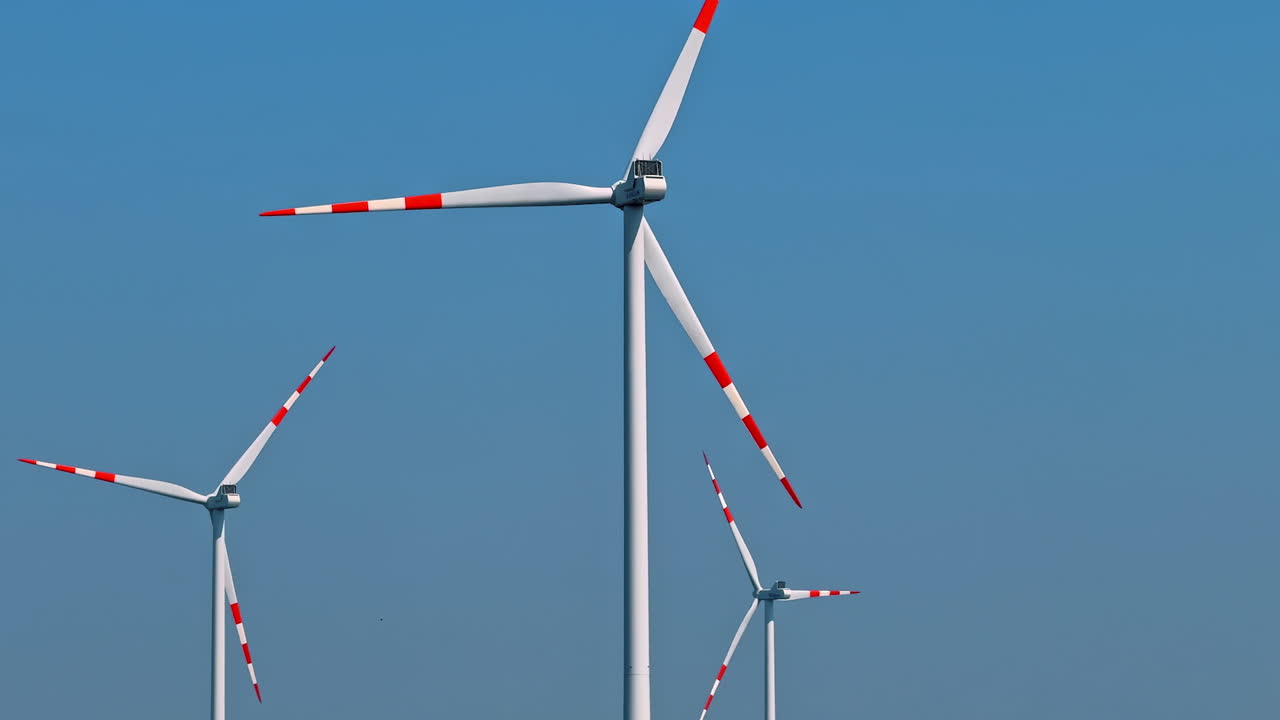 Wind turbines for renewable energy. Wind turbines with red and white blades stand against a clear blue sky, capturing wind energy in a rural landscape