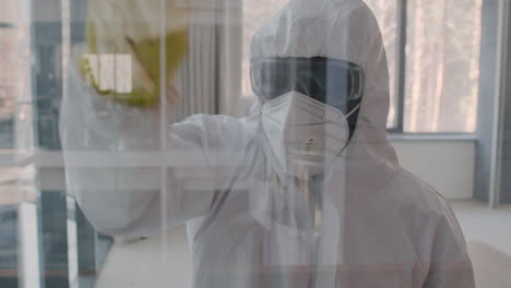 front view of a cleaning man wearing personal protective equipment cleaning window panes inside an office building 1