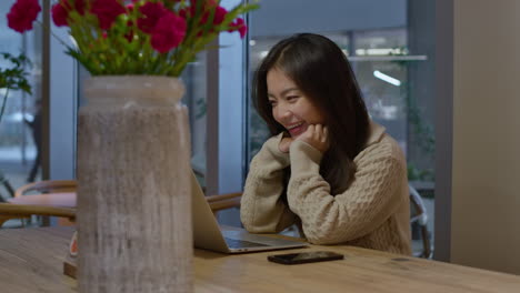 young pretty asian chinese girl talks happily and smiles during online call in cafe