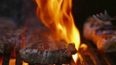 Grillflammen-In-Zeitlupe-Garen-Britische-Rinderlendensteaks,-Während-Der-Koch-Das-Fleisch-Aufhebt-Und-Umdreht,-Um-Es-Auf-Der-Anderen-Seite-Zu-Garen,-Wobei-Die-Würstchen-Sichtbar-Sind,-4k